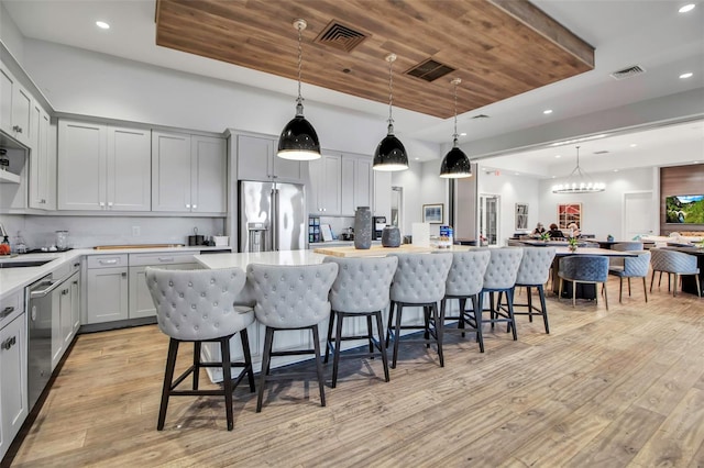 kitchen with stainless steel appliances, a raised ceiling, gray cabinets, light wood-style flooring, and recessed lighting
