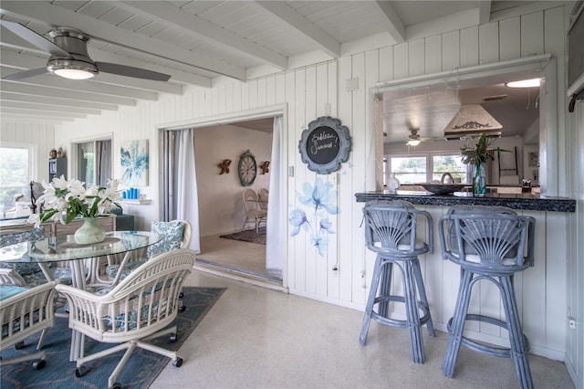 dining area featuring a ceiling fan, wood walls, and beam ceiling