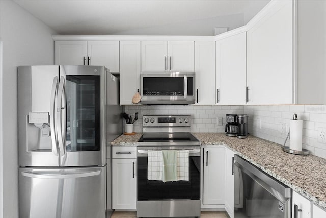 kitchen with appliances with stainless steel finishes, white cabinets, light stone countertops, and tasteful backsplash
