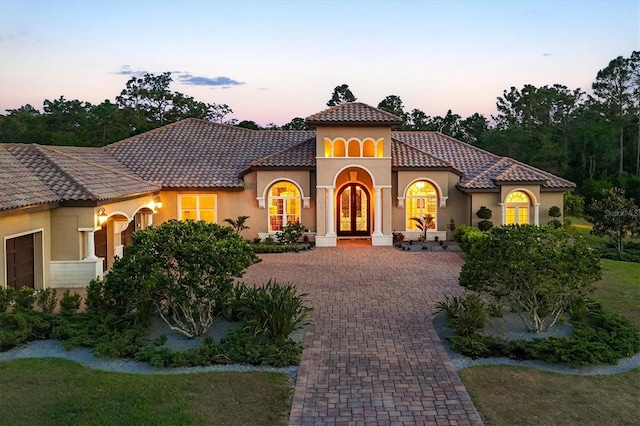 mediterranean / spanish-style home featuring a tiled roof, decorative driveway, french doors, and stucco siding
