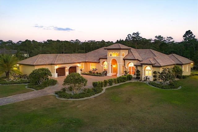 mediterranean / spanish house with a garage, stucco siding, a lawn, a tiled roof, and driveway