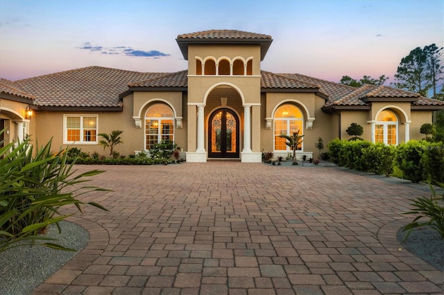 mediterranean / spanish home with french doors, stucco siding, a tiled roof, and decorative driveway