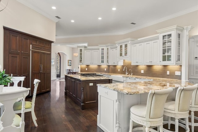 kitchen featuring arched walkways, a sink, dark wood finished floors, and white cabinetry