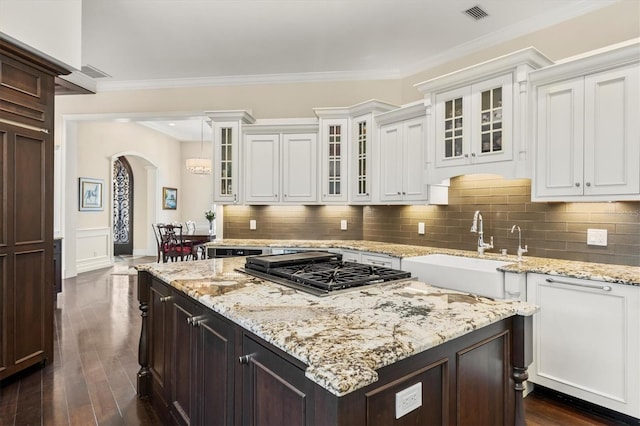 kitchen with visible vents, a kitchen island, arched walkways, a sink, and stainless steel gas stovetop