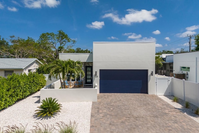 contemporary house featuring decorative driveway, fence private yard, stucco siding, and a gate