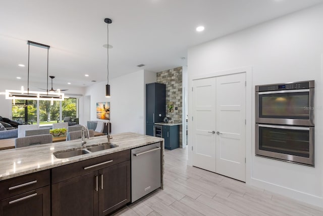 kitchen with dark brown cabinetry, light stone counters, stainless steel appliances, a sink, and open floor plan
