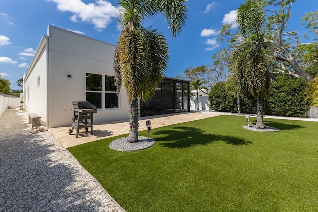 rear view of house featuring stucco siding, fence, a sunroom, a patio area, and a lawn