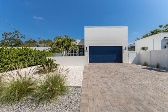 contemporary house featuring stucco siding, a gate, fence, decorative driveway, and a garage