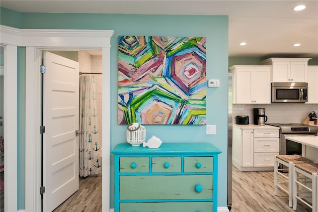 205 Elm Ave, Anna Maria, FL 34216 - kitchen with appliances with stainless steel finishes, white cabinetry, light wood-type flooring, and decorative backsplash