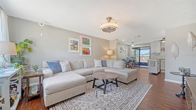 living area featuring ceiling fan, a textured ceiling, visible vents, wood finished floors, and baseboards