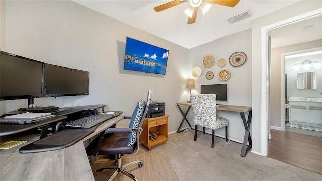 carpeted office space featuring ceiling fan, a sink, a textured ceiling, baseboards, and visible vents