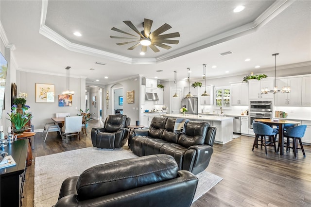 living room with dark wood-style flooring, visible vents, a raised ceiling, ceiling fan with notable chandelier, and ornamental molding