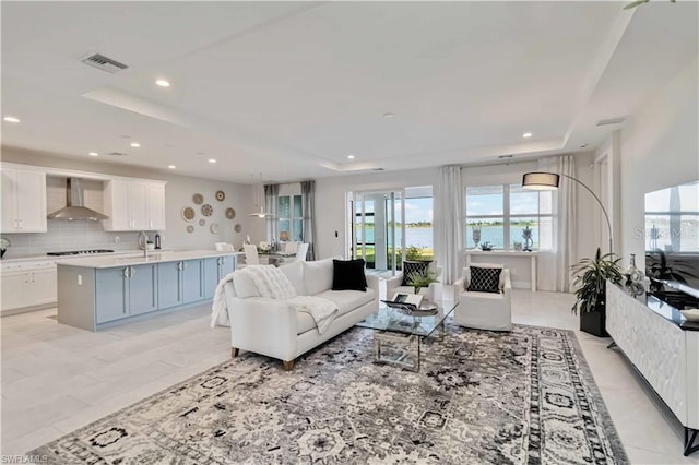 living room featuring a raised ceiling, recessed lighting, and visible vents