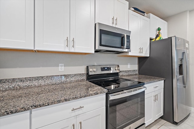 1723 Fred Ives St, Ruskin, FL 33570 - kitchen with white cabinets, appliances with stainless steel finishes, light tile patterned flooring, and dark stone counters