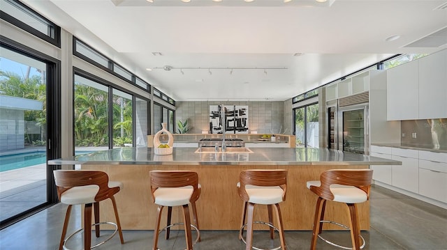 kitchen featuring tasteful backsplash, stainless steel counters, white cabinets, finished concrete flooring, and modern cabinets