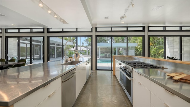 kitchen with stainless steel counters, modern cabinets, concrete flooring, stainless steel appliances, and white cabinets