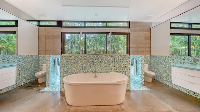 full bathroom with tile walls, toilet, a soaking tub, and vanity