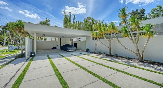 view of car parking featuring driveway, a carport, and fence