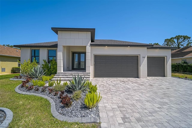 prairie-style house featuring stucco siding, decorative driveway, french doors, and an attached garage