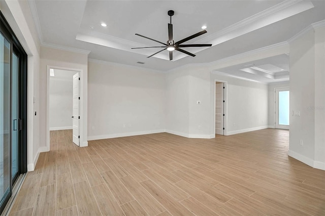 empty room with light wood finished floors, a tray ceiling, a ceiling fan, baseboards, and ornamental molding