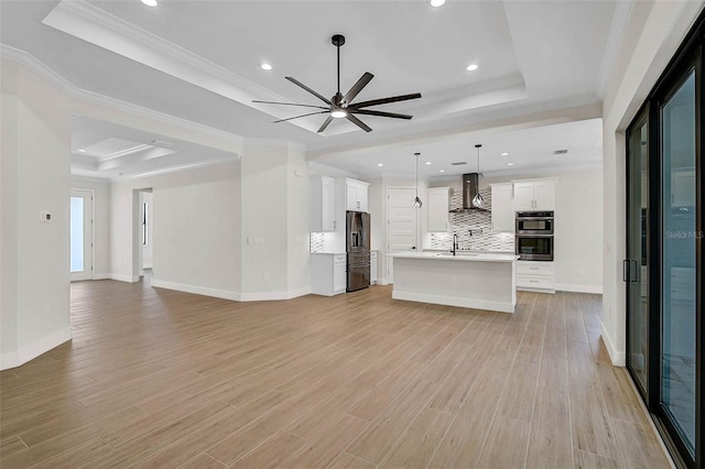 unfurnished living room featuring ceiling fan, a raised ceiling, baseboards, light wood-type flooring, and recessed lighting