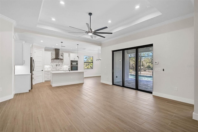 unfurnished living room featuring ceiling fan, baseboards, and a tray ceiling
