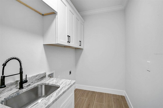 laundry area with cabinet space, a sink, baseboards, wood tiled floor, and crown molding