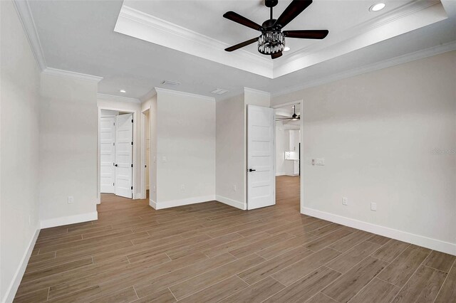 unfurnished bedroom featuring baseboards, wood finished floors, ornamental molding, and a tray ceiling