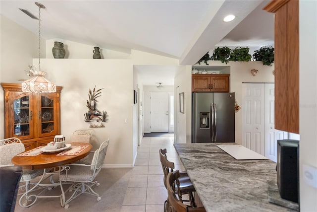kitchen with brown cabinets, baseboards, stainless steel refrigerator with ice dispenser, light tile patterned flooring, and lofted ceiling