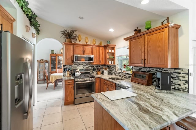 kitchen featuring light tile patterned floors, a sink, appliances with stainless steel finishes, a peninsula, and backsplash