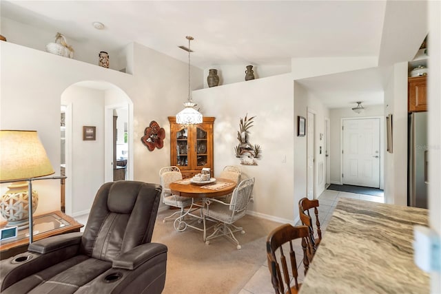 dining space featuring arched walkways, light colored carpet, light tile patterned floors, baseboards, and lofted ceiling