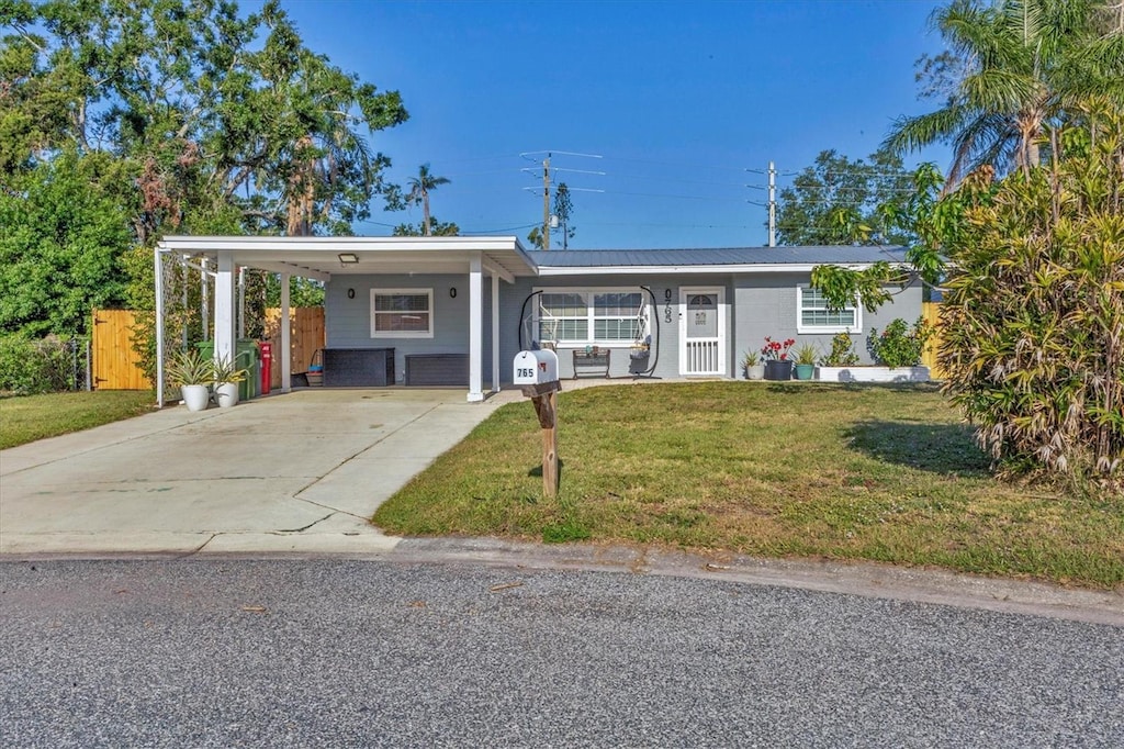 ranch-style house with a front lawn, an attached carport, metal roof, driveway, and fence