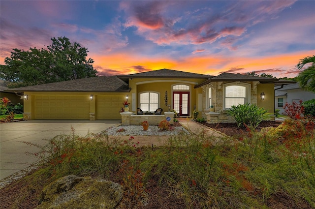 view of front facade featuring driveway, french doors, a garage, stone siding, and stucco siding