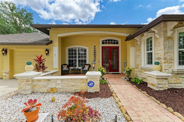 entrance to property with an attached garage, stone siding, a porch, french doors, and driveway