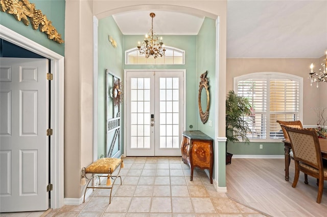 foyer entrance featuring french doors, arched walkways, baseboards, and a chandelier