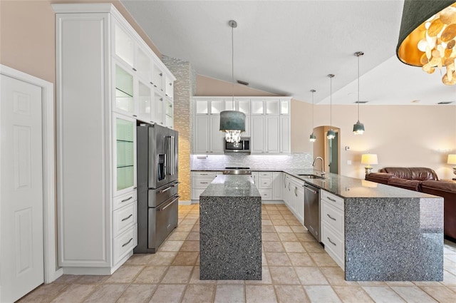 kitchen featuring appliances with stainless steel finishes, a peninsula, tasteful backsplash, vaulted ceiling, and glass insert cabinets