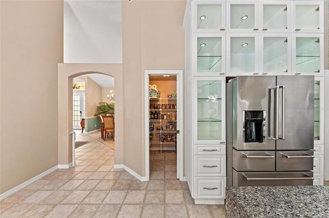 kitchen featuring arched walkways, dark stone countertops, white cabinetry, baseboards, and stainless steel refrigerator with ice dispenser