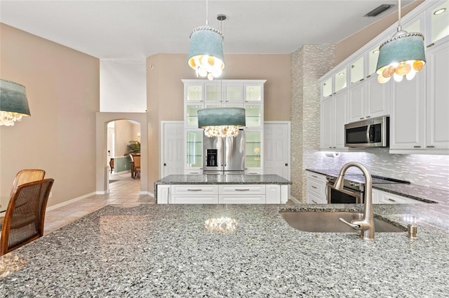 kitchen with decorative backsplash, a sink, dark stone counters, arched walkways, and appliances with stainless steel finishes
