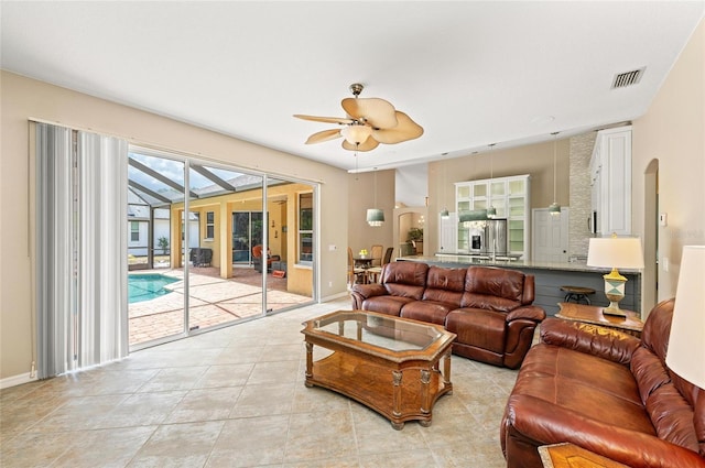 living room featuring arched walkways, ceiling fan, a sunroom, and visible vents