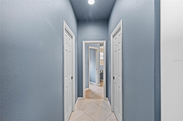 hall with baseboards, a textured wall, and light tile patterned floors