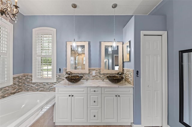 bathroom with a sink, an inviting chandelier, a garden tub, and double vanity