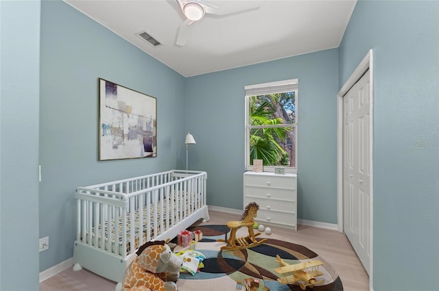 bedroom featuring a closet, wood finished floors, baseboards, ceiling fan, and a crib