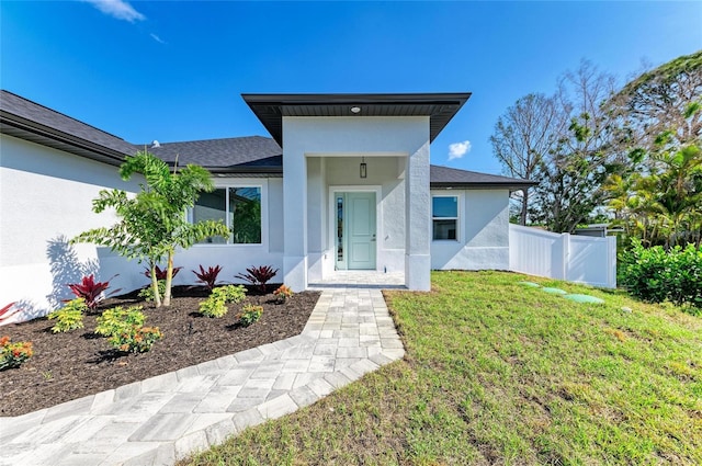 doorway to property with fence, stucco siding, roof with shingles, and a lawn