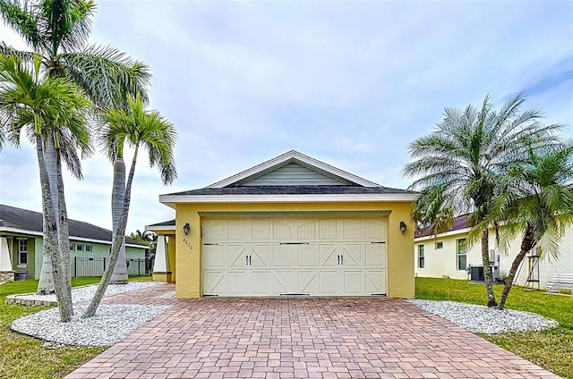 garage featuring fence, central AC, and decorative driveway