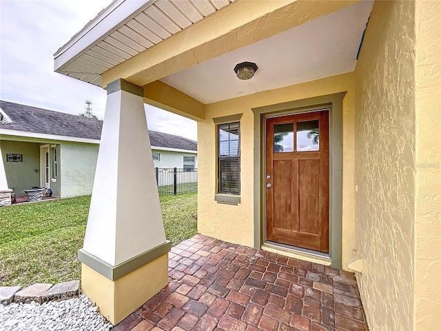 doorway to property featuring stucco siding, fence, and a yard