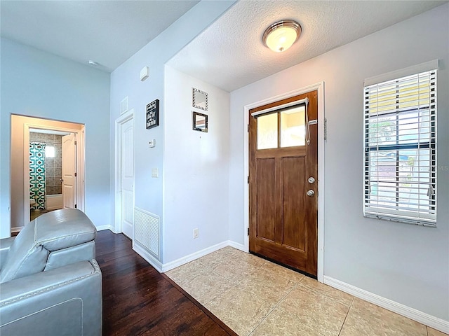 foyer featuring baseboards, wood finished floors, and visible vents