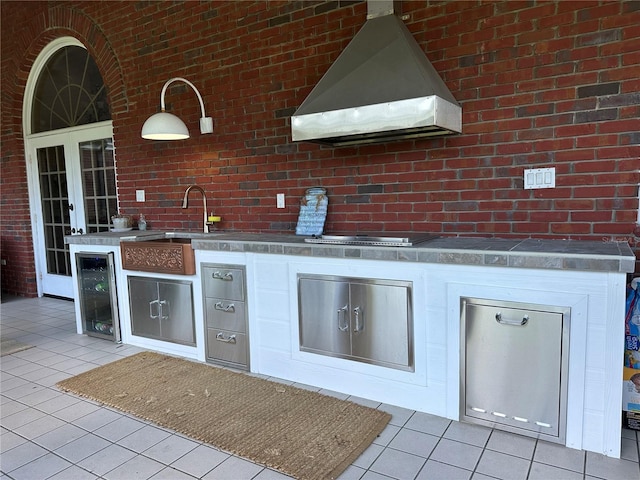 708 E Main St, Wauchula, FL 33873 - kitchen with wine cooler, light tile patterned floors, brick wall, a sink, and wall chimney exhaust hood