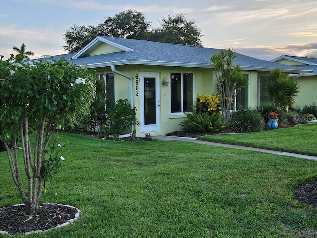 ranch-style house featuring a yard, stucco siding, and a shingled roof