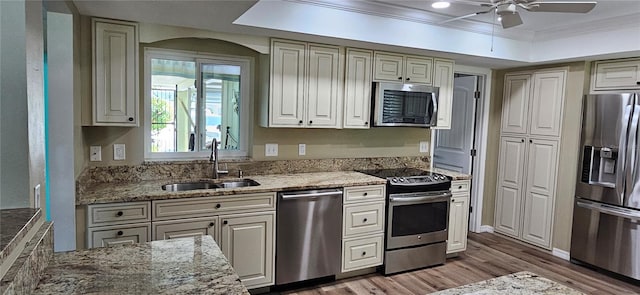 kitchen featuring a sink, stainless steel appliances, light stone counters, ceiling fan, and light wood-style floors