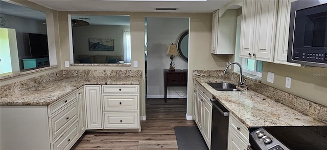 kitchen with a sink, stainless steel appliances, wood finished floors, light stone counters, and white cabinetry